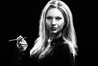 Portrait of young woman holding stick against black background