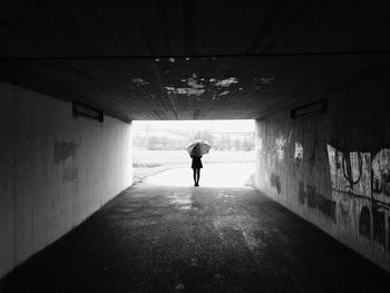 Rear view of woman standing with umbrella in tunnel