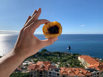 Person holding cake by sea against sky