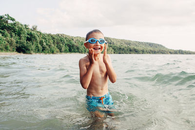 Full length of shirtless boy in sea against sky