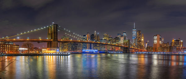 Illuminated city by river against sky at night