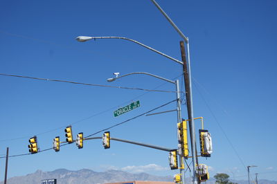 Low angle view of street lights and traffic signal against clear blue sky