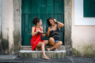 Portrait of two beautiful and happy girls sitting against a green colored door.