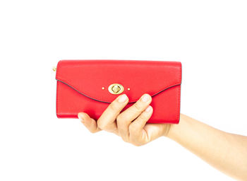 Close-up of cropped hand holding red purse over white background