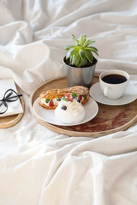 Cakes, coffee cup, notebook and eyeglass on wooden tray on bedding. cozy breakfast in bed.