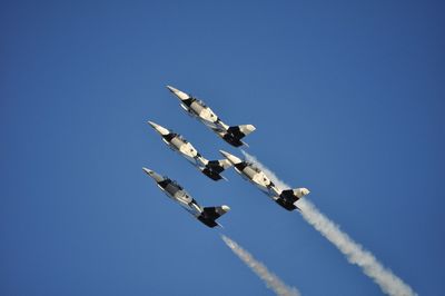 Low angle view of military aircrafts with trails against clear blue sky