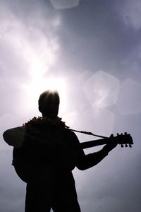 Silhouette guitarist playing guitar against sky