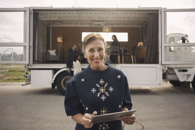 Portrait of smiling businesswoman holding digital tablet with colleagues and portable office truck in background