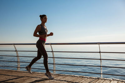 Side view of young woman standing by railing against sea