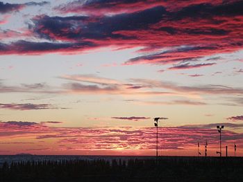 Silhouette people on field against dramatic sky during sunset