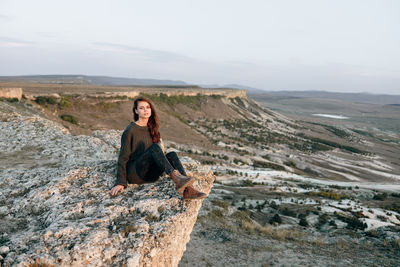 Portrait of young woman sitting on rock against mountain