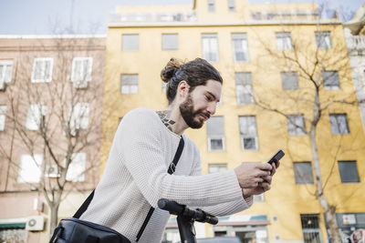 Young man using smart phone against building in city