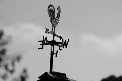 Low angle view of weather vane against cloudy sky