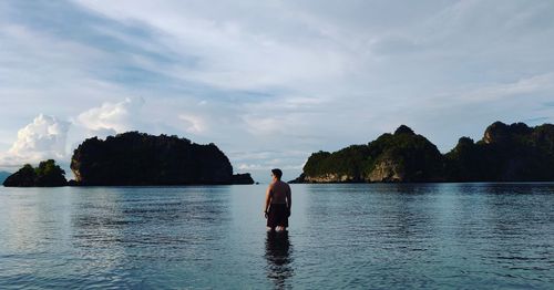 Rear view of shirtless man standing in sea against sky