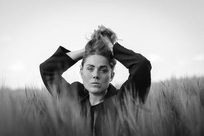Portrait of young woman looking at camera on field against sky