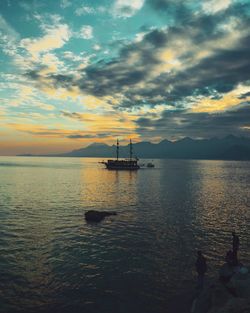 Sailing ship in sea against cloudy sky during sunset