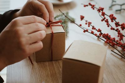 Cropped hands of person tying small cardboard box on table