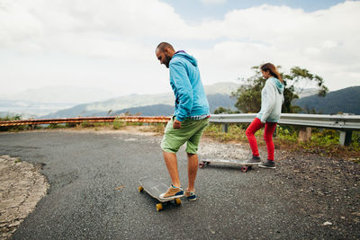 Couple skateboarding on road against sky