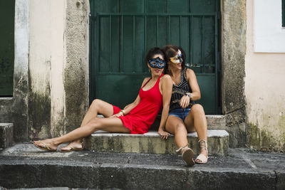 Portrait of two seated women wearing mask against green door.