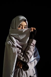 Portrait of young woman wearing headscarf against black background