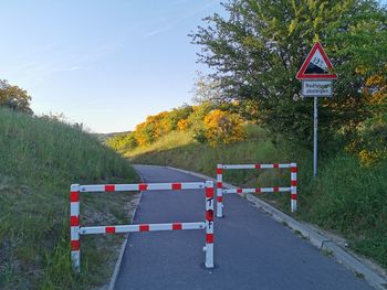 Road sign by trees against sky