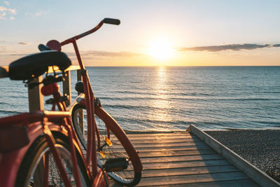 Bicycle by sea against sky during sunset