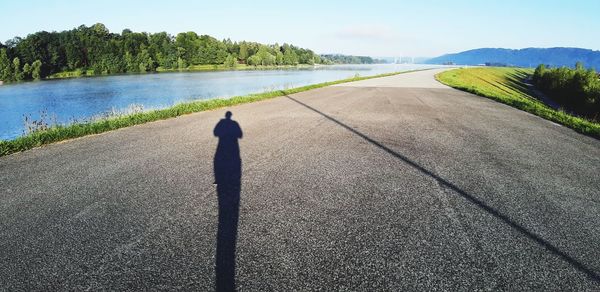 Shadow of woman standing on road against sky