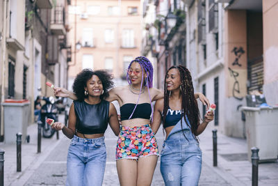 Cheerful female friends walking on street amidst buildings in city