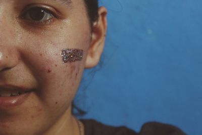 Cropped portrait of woman with glitter on face against blue wall