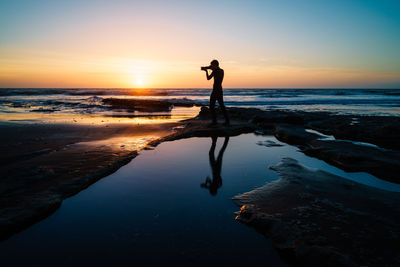 Silhouette man standing on beach against sky during sunset