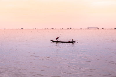 Silhouette man in boat in sea against sky during sunset