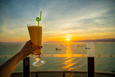 Close-up of hand holding wine glass against sunset