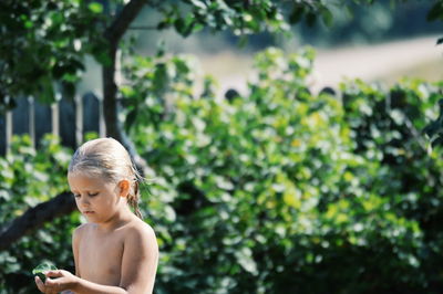 Shirtless girl holding leaf standing against plants