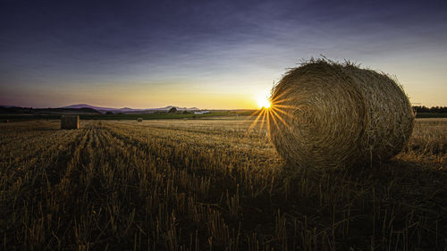 Hay bales on field against sky during sunset