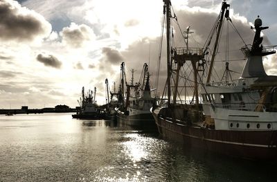 Boats in harbor against cloudy sky