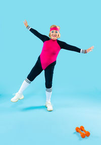 Low angle view of woman with arms raised against blue background