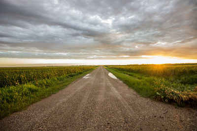 Road amidst field against sky during sunset