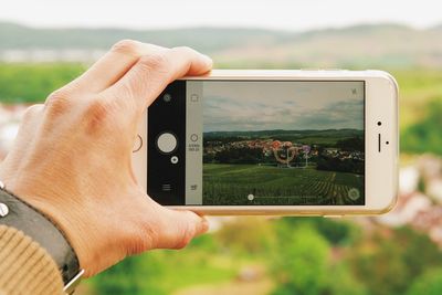 Cropped image of man photographing landscape from mobile phone