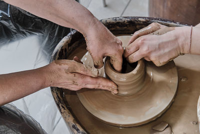 Hands of senior woman and girl sculpting clay vase on potter's wheel at pottery training lesson.