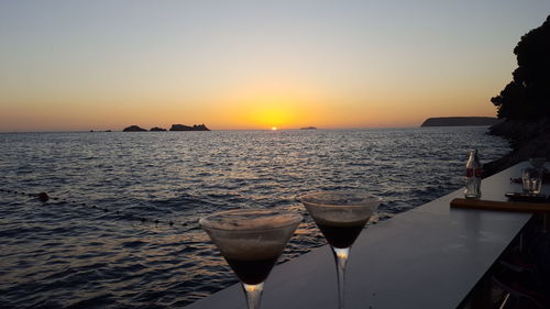 Close-up of beer in sea against sunset sky