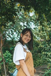 Portrait of smiling young woman standing against trees