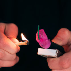 Midsection of person holding burning candle against black background