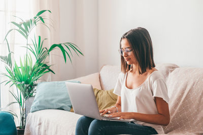Young woman using laptop while sitting on bed at home
