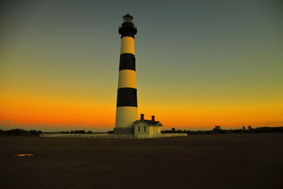 Lighthouse by sea against sky during sunset