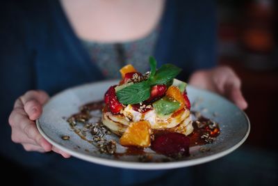 Midsection of woman holding pancake in plate