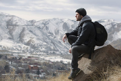 Side view of young man sitting on rock