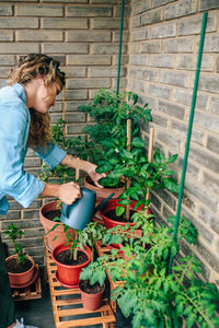 Woman using watering can with plants of urban garden on terrace