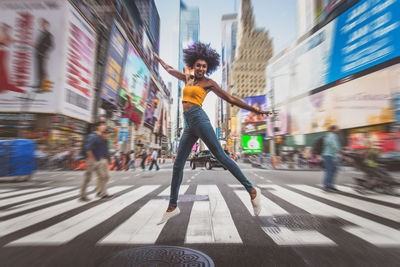 Full length of excited young woman dancing on zebra crossing in city