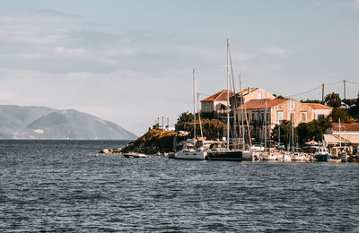 Sailboats in sea by buildings against sky