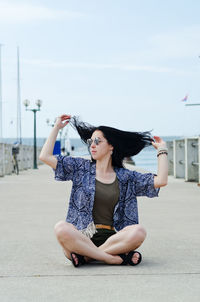 Full length of young woman with arms raised against sky